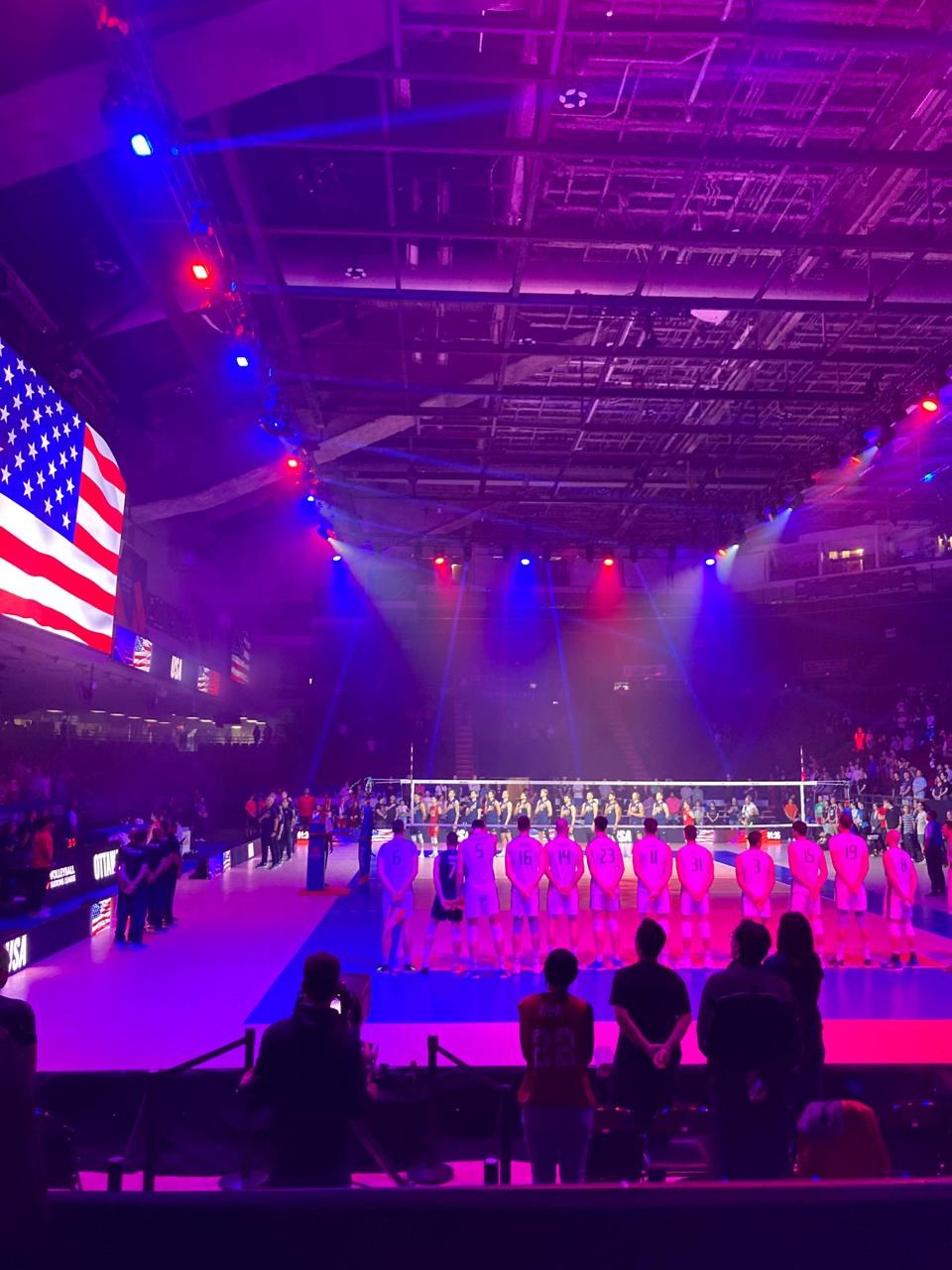 Team lined up for the national anthem before a match, American flag lit up behind them