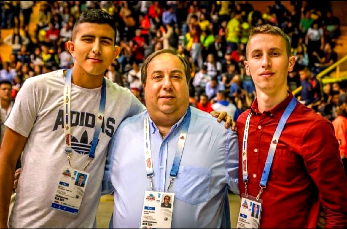Luis Zuluaga with two colleagues courtside at a volleyball championship, wearing event credentials